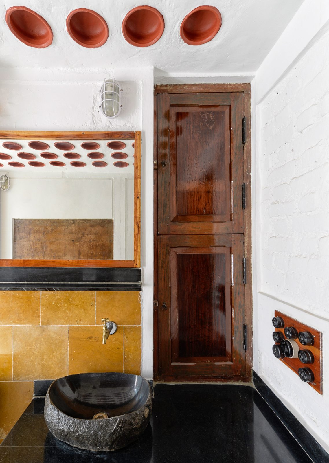 Rammed earth farm house, Thane, Mumbai: bathroom stone basin yellow tiles, interior photograph.