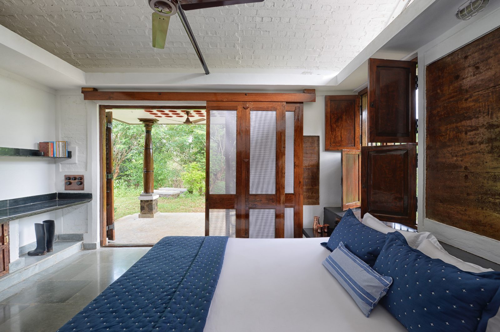 Rammed earth farm house, Thane, Mumbai: bedroom blue bed teak shutters, interior photograph.